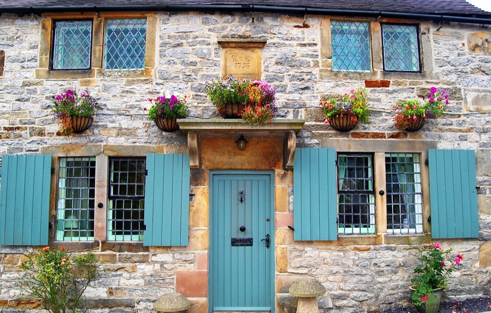 The stone front of an old school house in Derbyshire with leaded windows and painted shutters